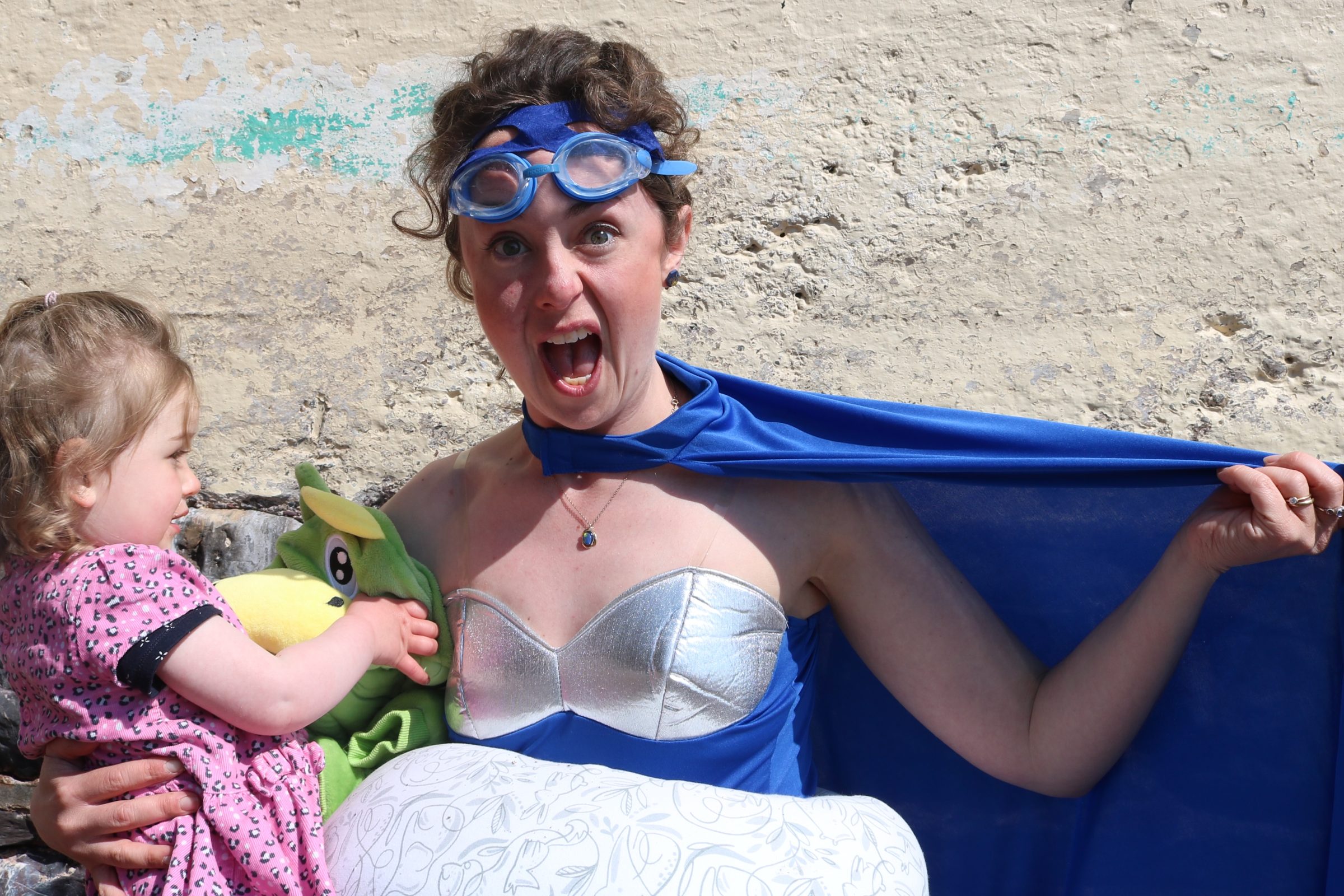 A mother in a superhero outfit stretches her cape and pulls a 